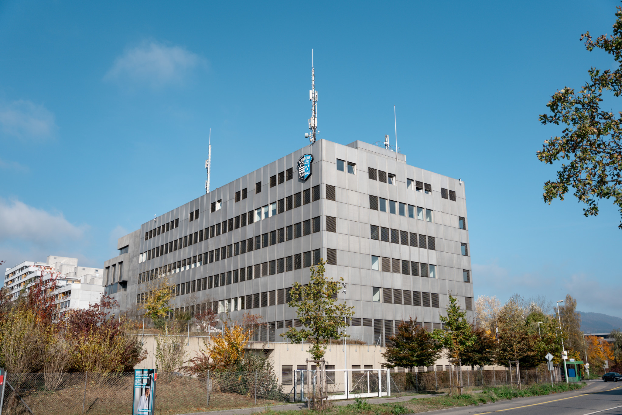 Mehrstöckiges Gebäude der Kantonspolizei Aargau in Aarau mit Antennen auf dem Dach und blauem Polizeilogo.