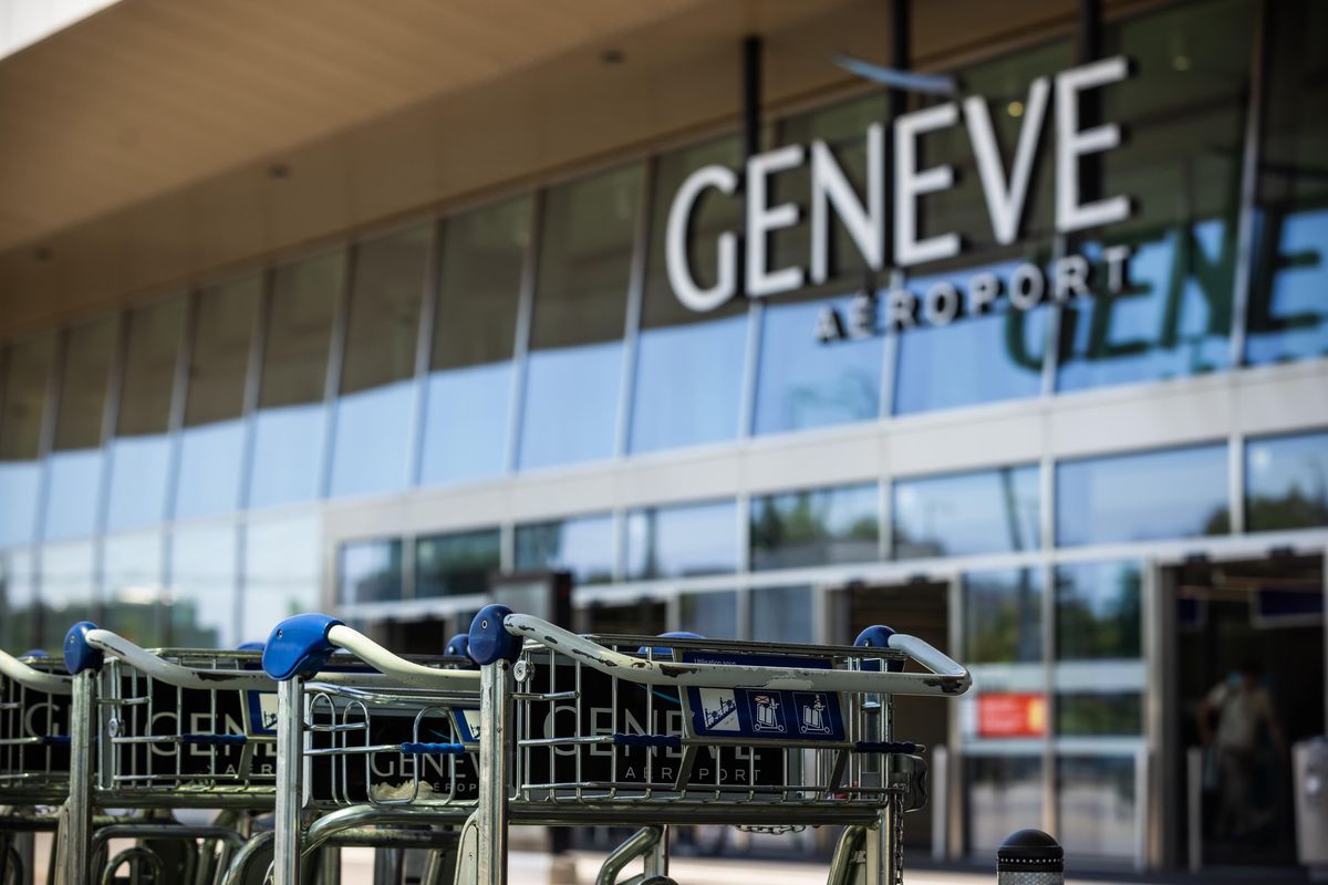 Chariots à bagages devant l'entrée de l'aéroport de Genève avec enseigne 'Genève Aéroport' en arrière-plan.
