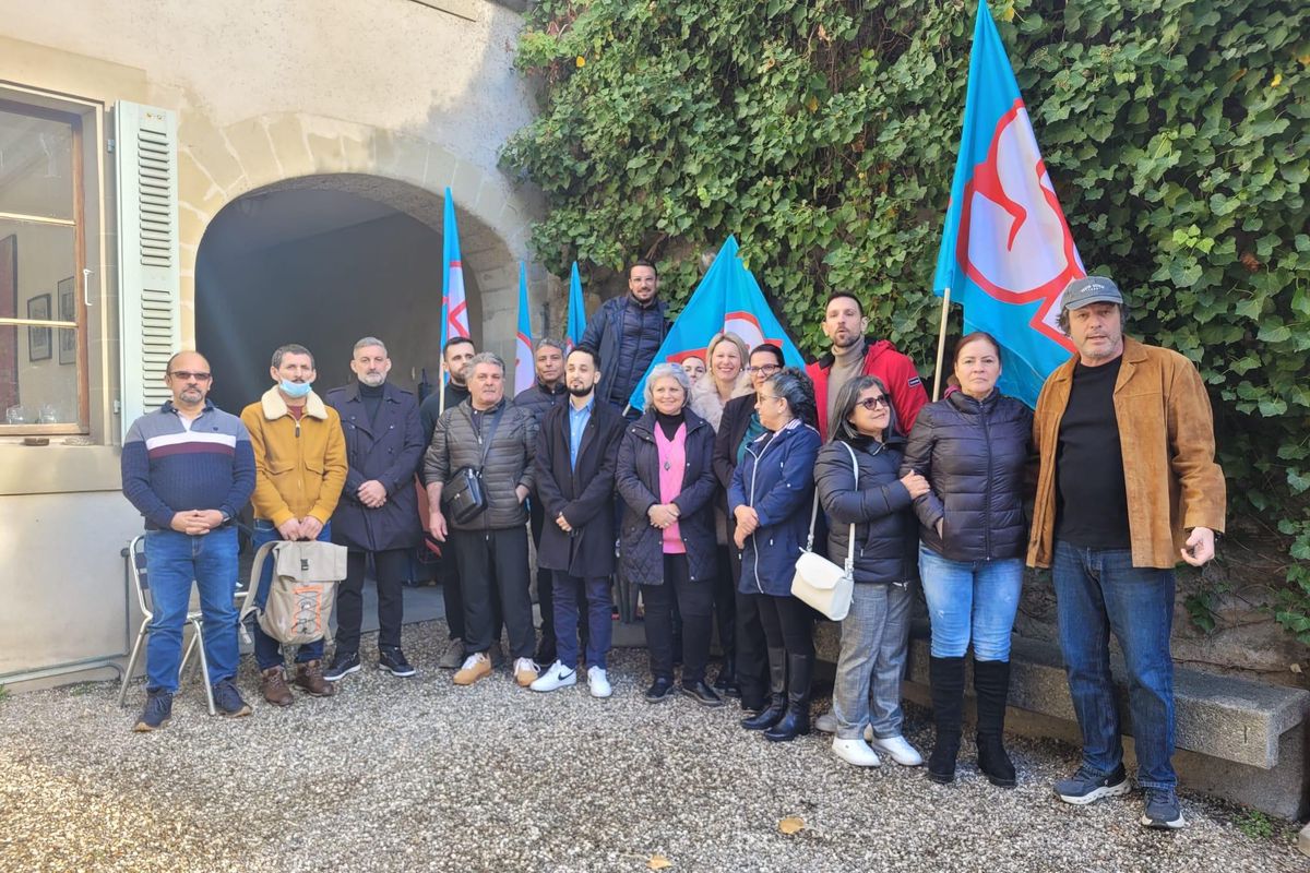 Groupe de personnes debout devant un bâtiment, tenant des drapeaux bleus avec des logos rouges.