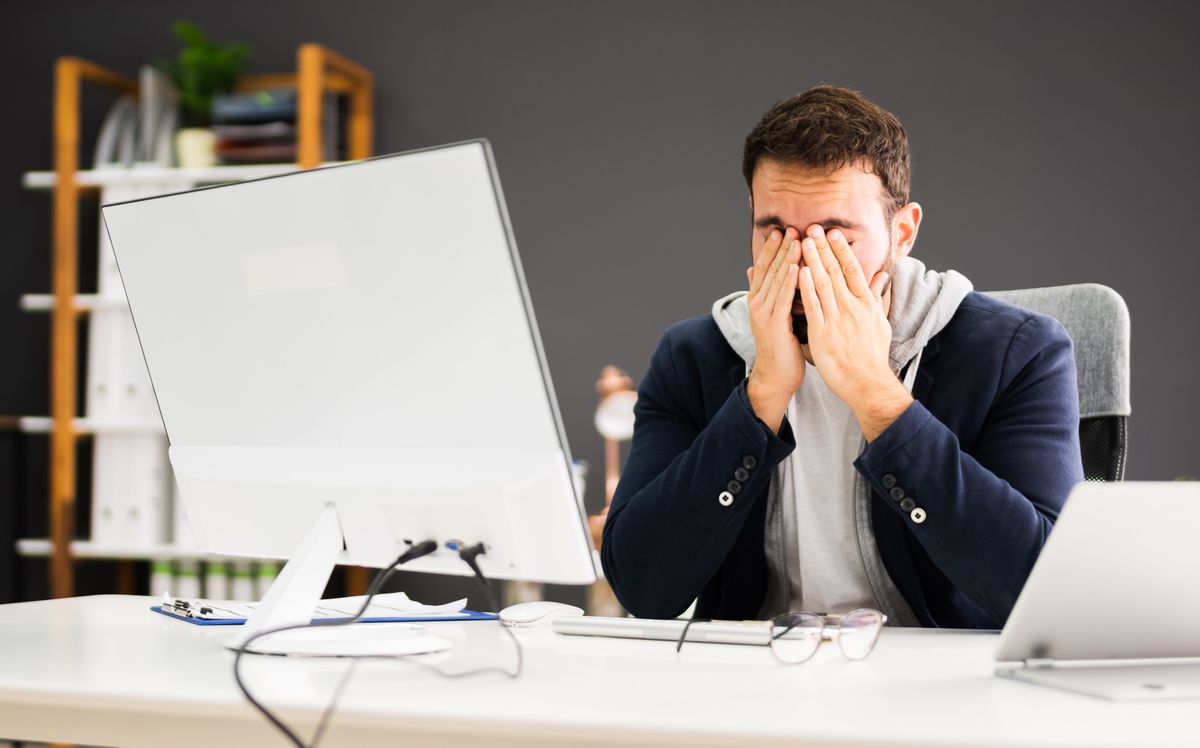 Homme fatigué et stressé, assis devant un ordinateur, se tenant la tête avec les mains.