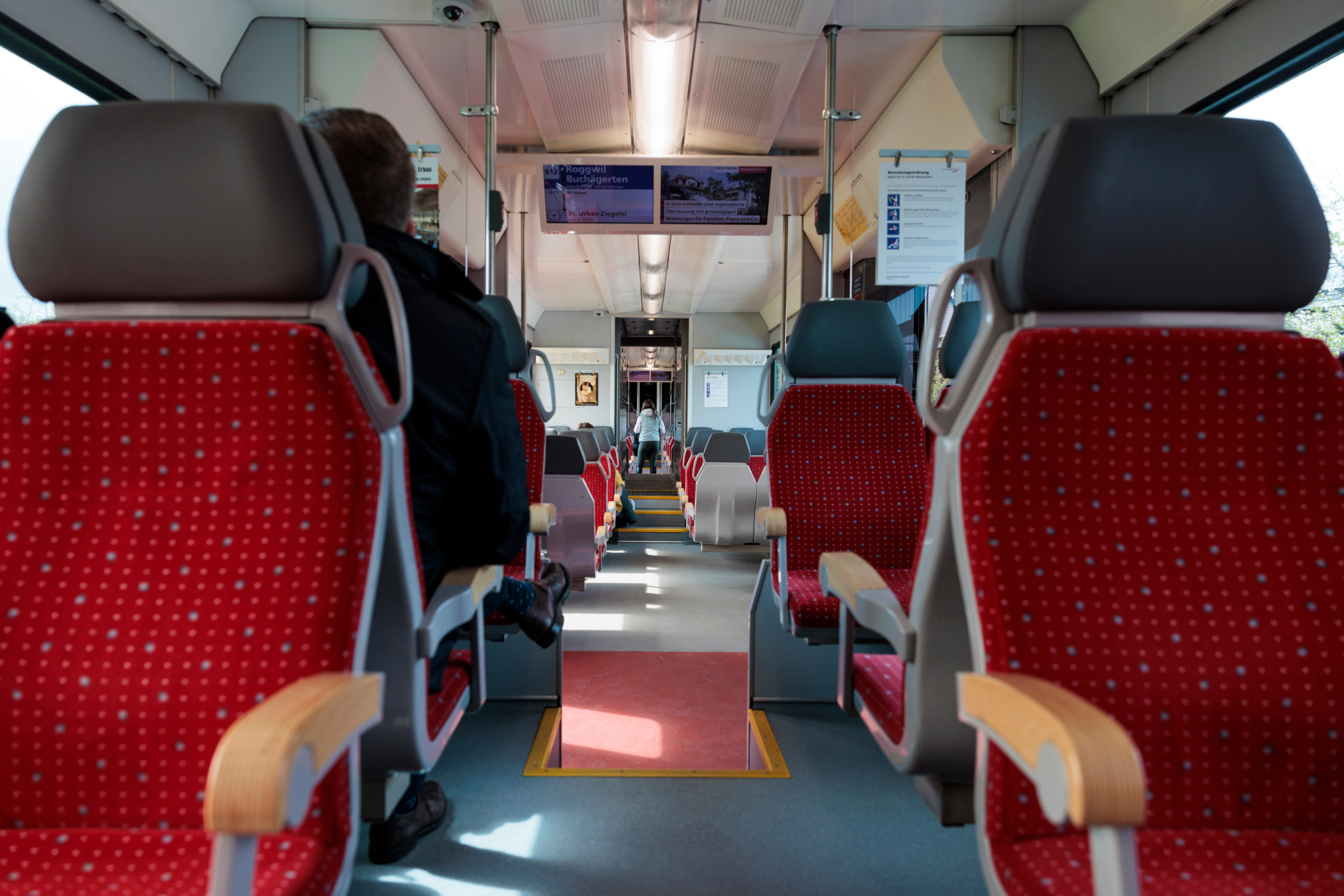 Innenansicht eines GTW-Zugs auf dem Bahnhof Langenthal mit roten Sitzen und wenigen Passagieren. Datum: 18. April 2024.