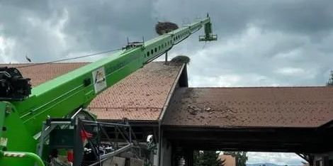 Grue verte soulevant des matériaux sur le toit d'un bâtiment sous un ciel nuageux.