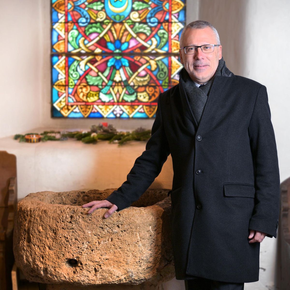 Le diacre Pierre-Alain Mischler dans le temple de Vers-l’Eglise, devant un vitrail coloré, le 13 décembre 2024.