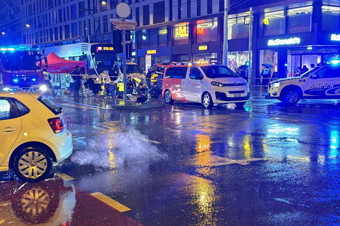 Scène de rue la nuit, montrant une intersection mouillée avec des lumières de voiture et des reflets colorés sur la chaussée.