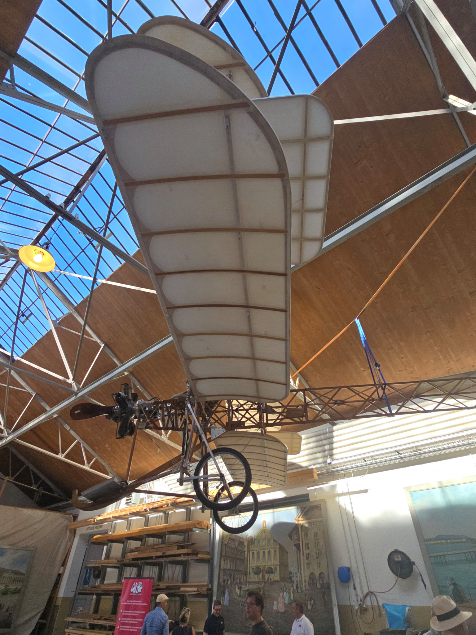 Un ancien avion biplan exposé dans un hangar avec des poutres métalliques et une verrière.