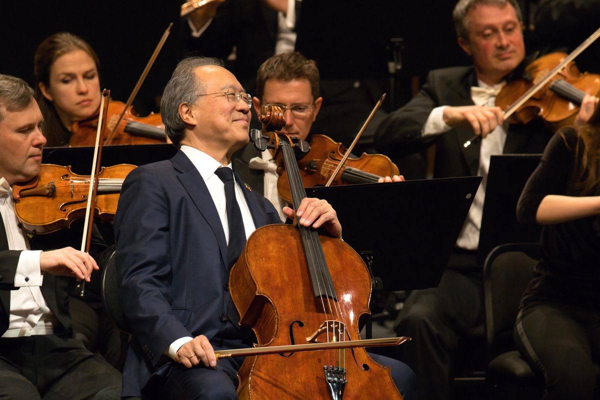 Un violoncelliste souriant joue avec un orchestre sur scène.