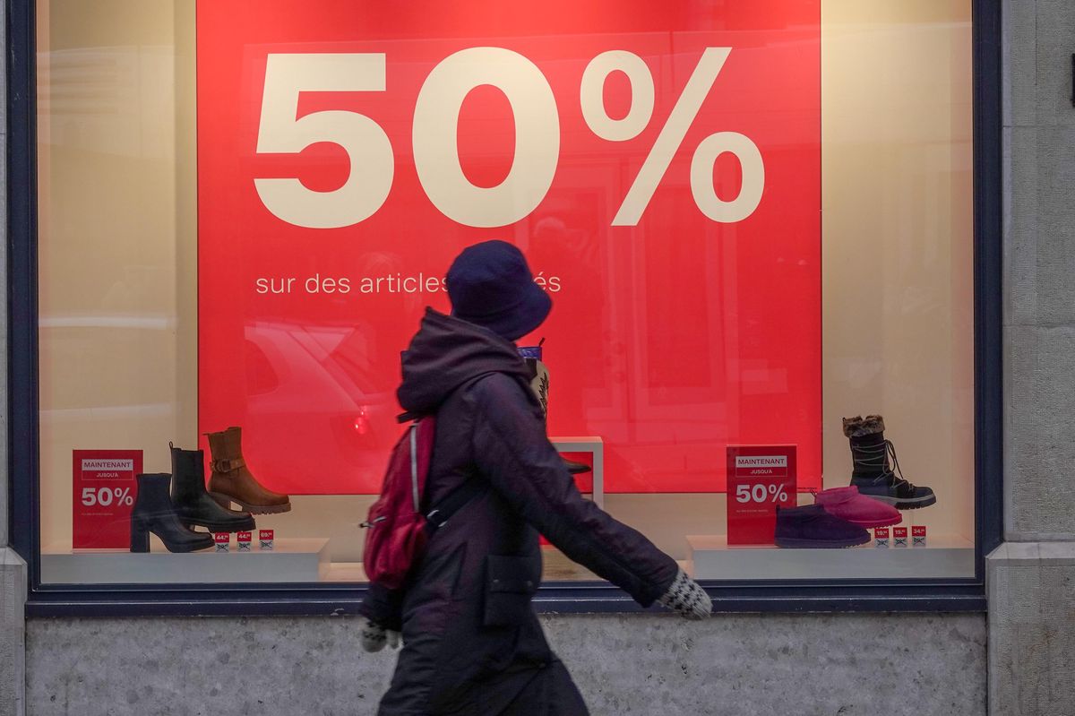Vitrine à Genève annonçant des soldes jusqu’à 50 % sur les articles, avec une personne passant devant en manteau et chapeau.