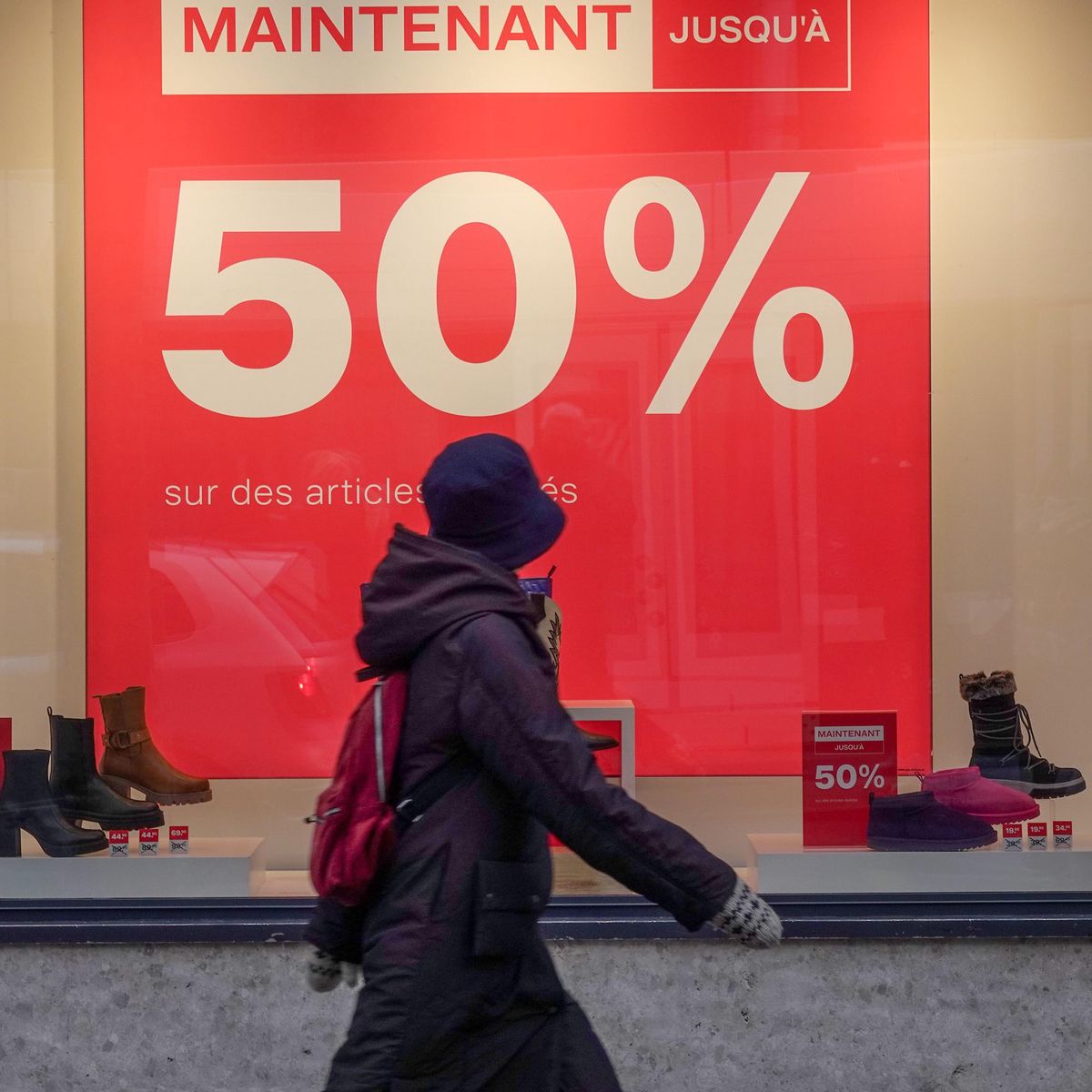 Vitrine à Genève annonçant des soldes jusqu’à 50 % sur les articles, avec une personne passant devant en manteau et chapeau.