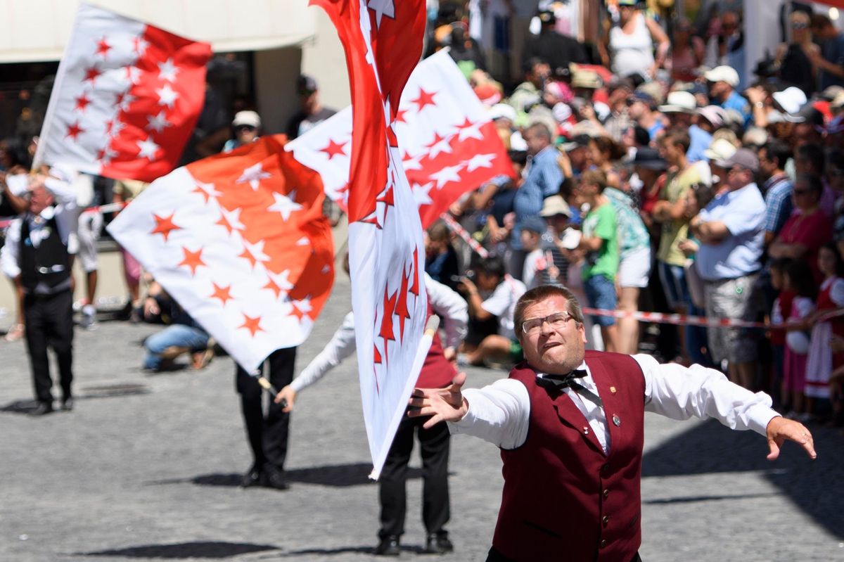 Une personne en costume traditionnel lance un drapeau valaisan lors du cortège de la 30ème édition de la Fête fédérale de jodle à Brigue, Valais.