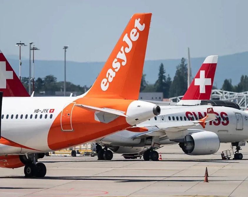 Avions de compagnie aérienne easyJet et Swiss stationnés sur le tarmac d'un aéroport, avec des montagnes visibles en arrière-plan.