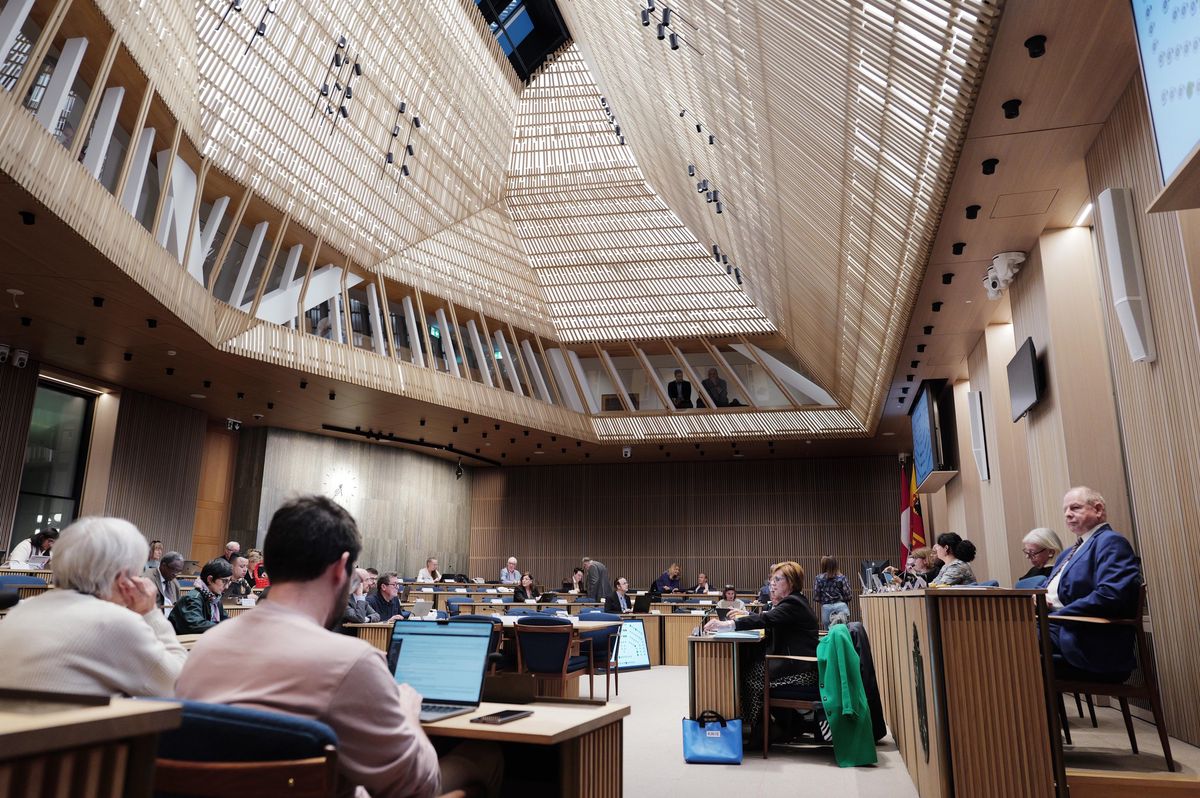 Réunion du Conseil municipal de Genève à l’Hôtel de Ville, montrant des participants assis dans une salle moderne avec un plafond en bois.