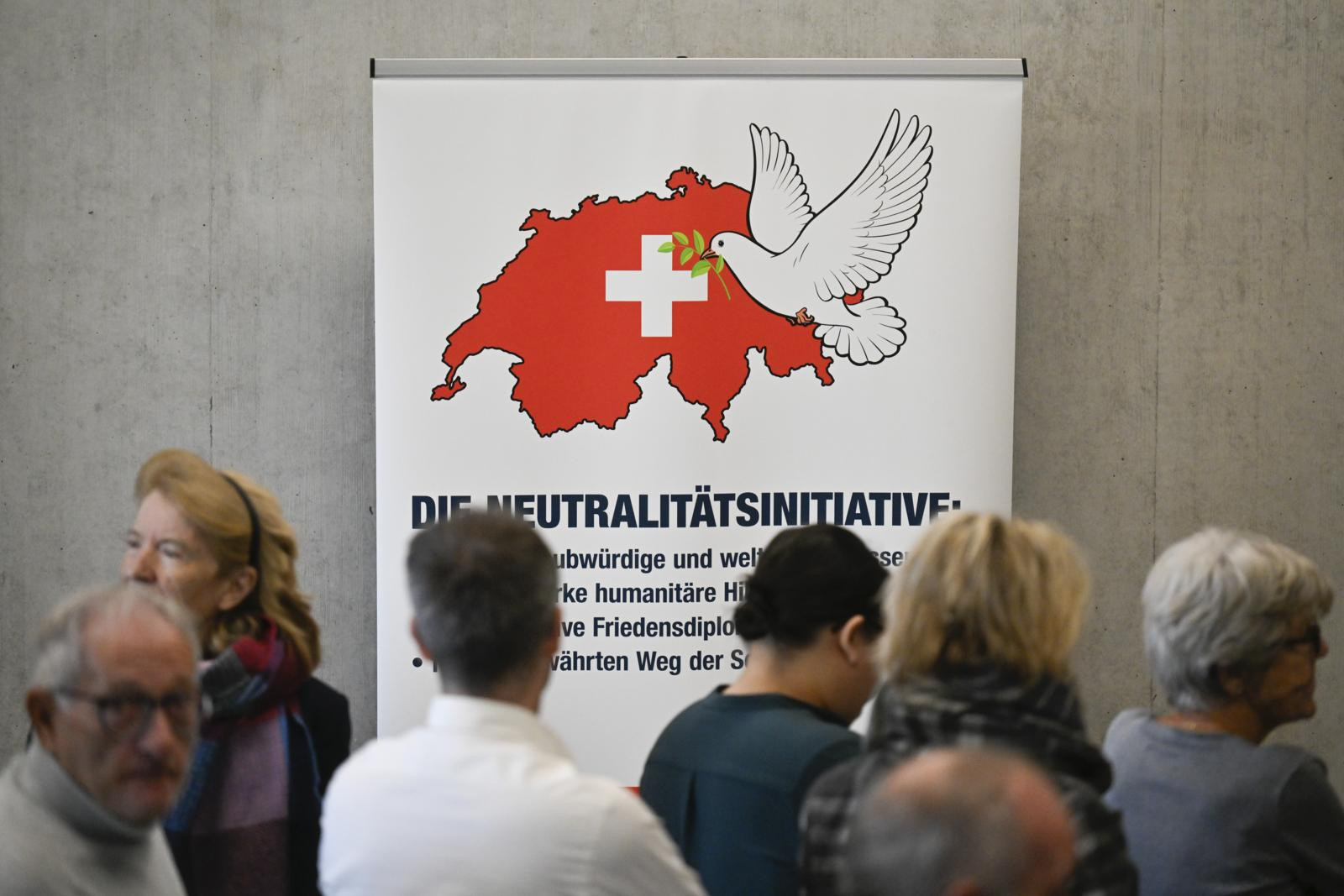 Mehrere Personen vor einem Banner der Neutralitätsinitiative mit Schweizer Karte, weissem Kreuz und Friedenstaube.