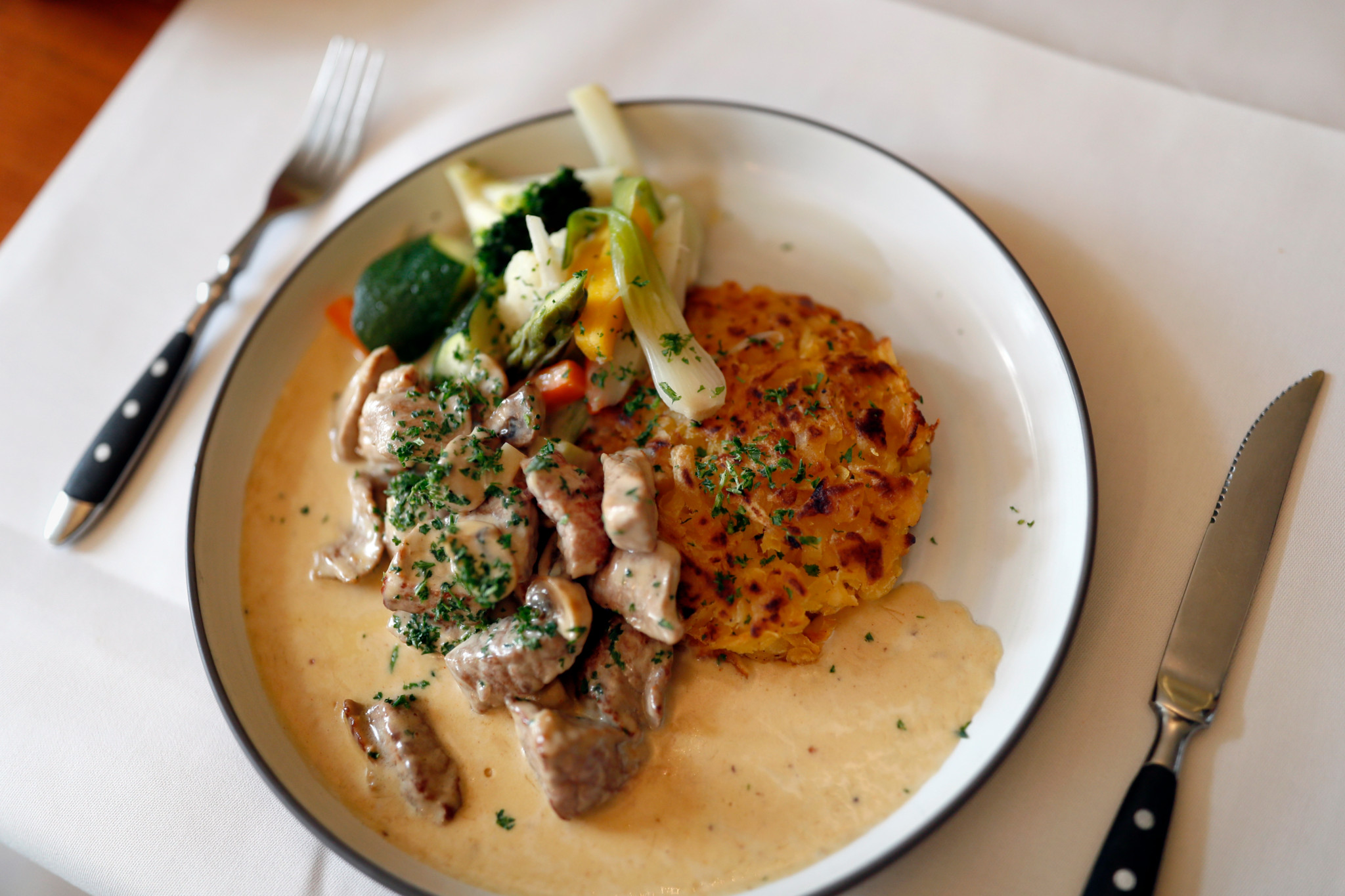 Ein Teller mit Kalbfleisch in Rahmsauce, serviert mit Rösti und einem Gemüsebouquet im Restaurant Frieden in Niederhasli, Zürich.