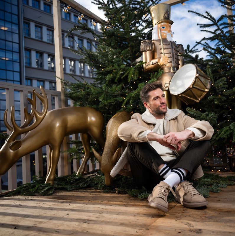 Steven Epprecht sitzt neben einer goldenen Rentierstatue auf einer weihnachtlich geschmückten Terrasse, umgeben von Tannenbäumen.