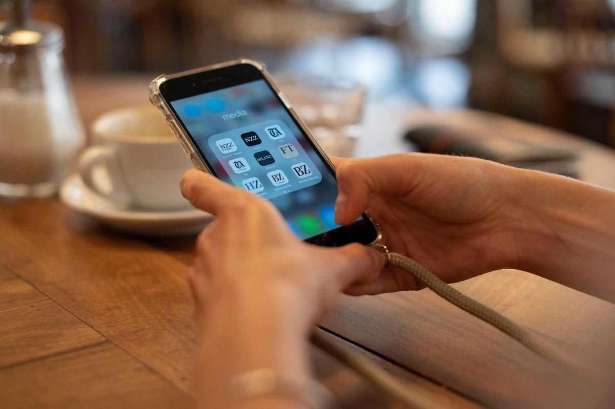 Personne tenant un smartphone affichant des applications de réseaux sociaux sur l'écran, avec une tasse de café en arrière-plan.