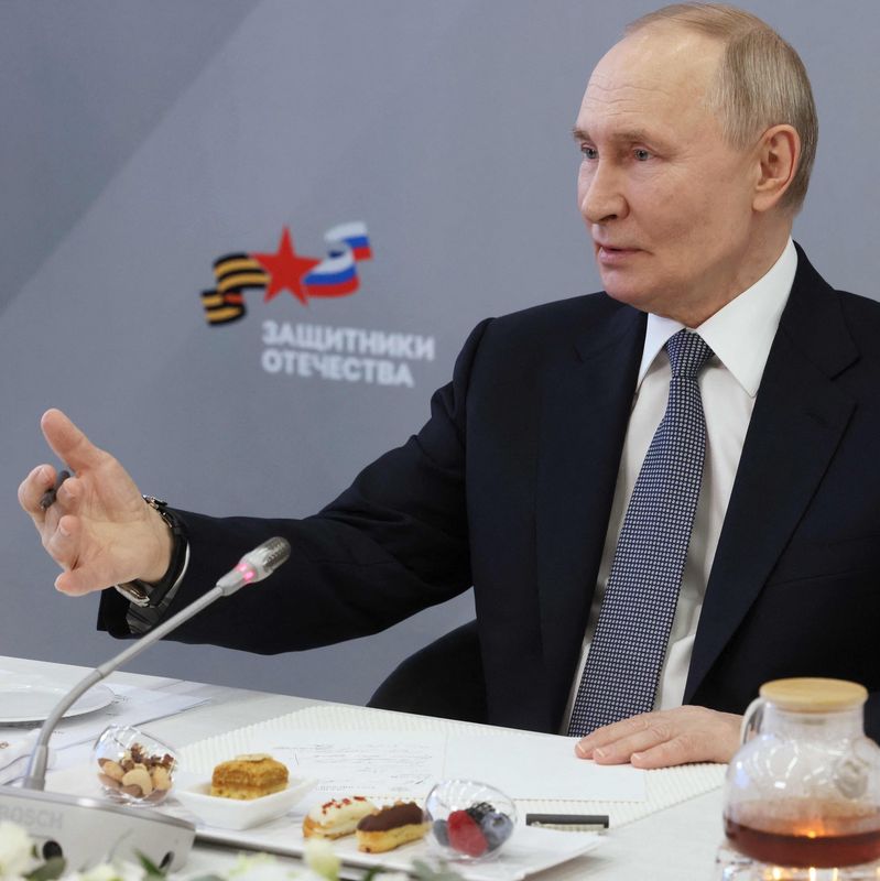 Le président russe Vladimir Poutine rencontre des travailleurs et bénéficiaires du Fonds d’État des Défenseurs de la Patrie à Moscou le 6 mars 2025, discutant à une table avec des desserts et une théière devant lui.
