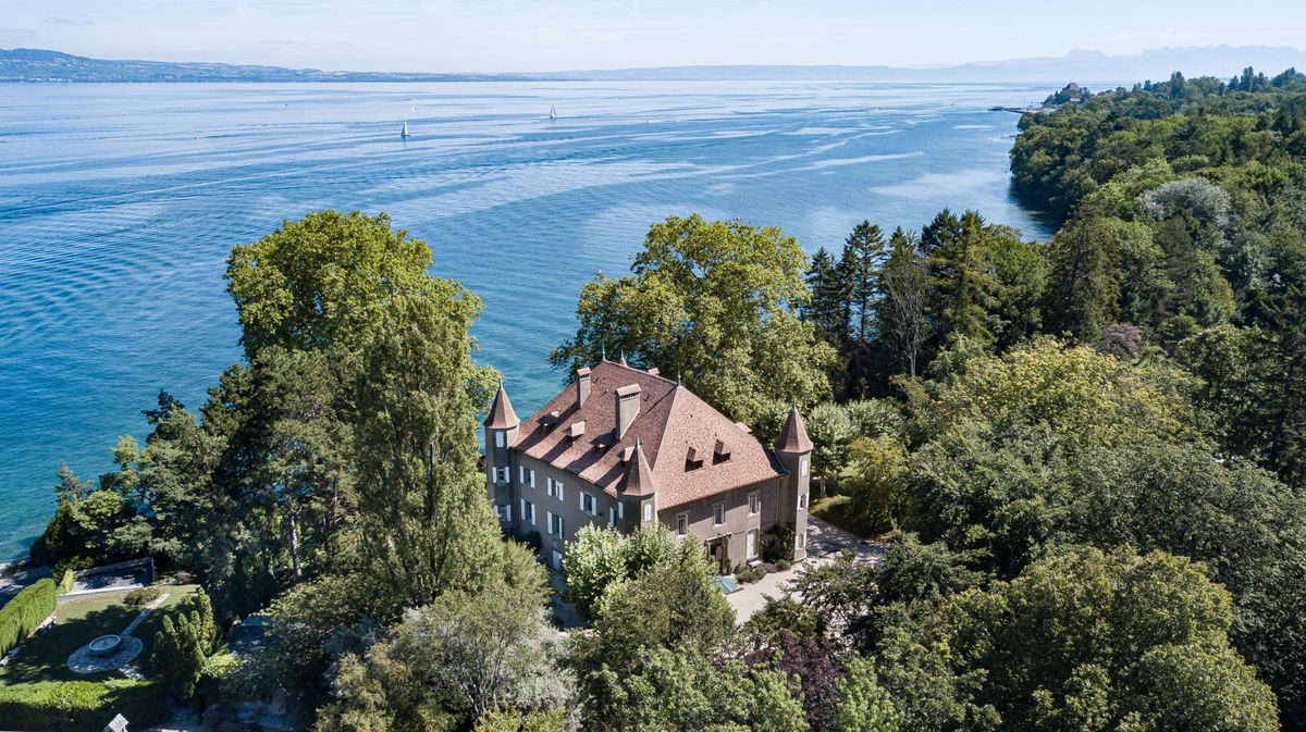 Vue aérienne d'un château entouré de verdure au bord du lac Léman.