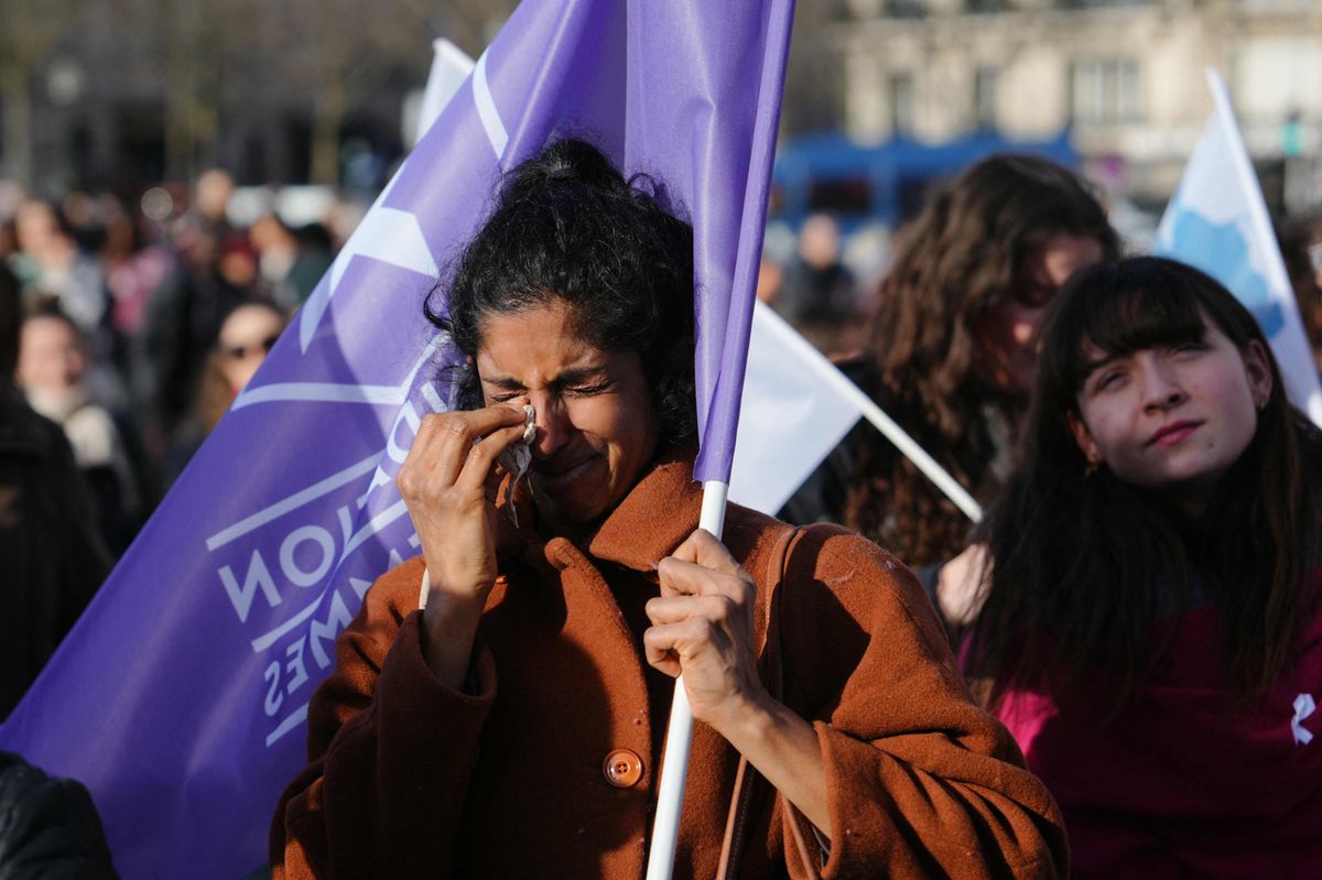 Une femme verse des larmes en tenant un drapeau de la "Fondation des Femmes", groupe de défense des droits des femmes, alors que des personnes se rassemblent sur la place du Trocadéro à Paris, le 4 mars 2024, lors de la diffusion de la convocation des deux chambres du Parlement pour ancrer le droit à l'avortement dans la constitution du pays. 