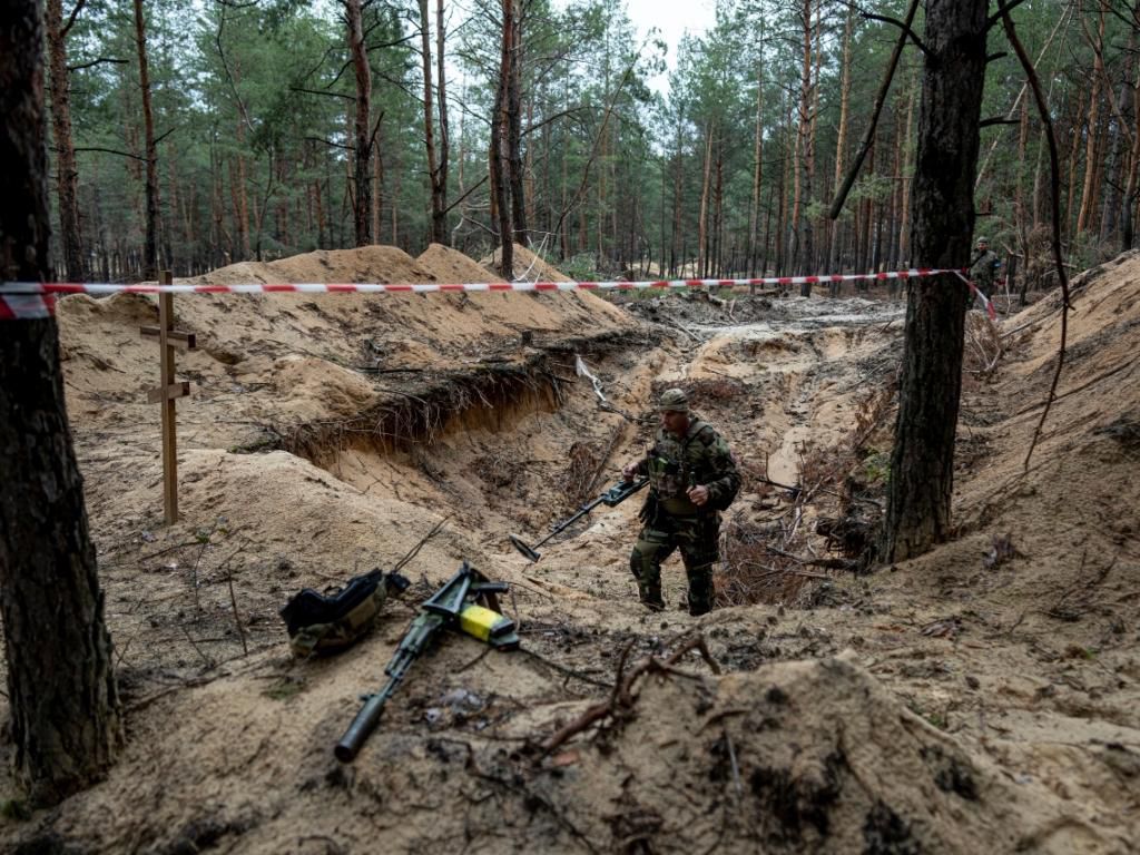 Ukrajinský voják pomocí detektoru kovů prohlíží hromadný hrob v nedávno znovu dobytém městě Izjum. 