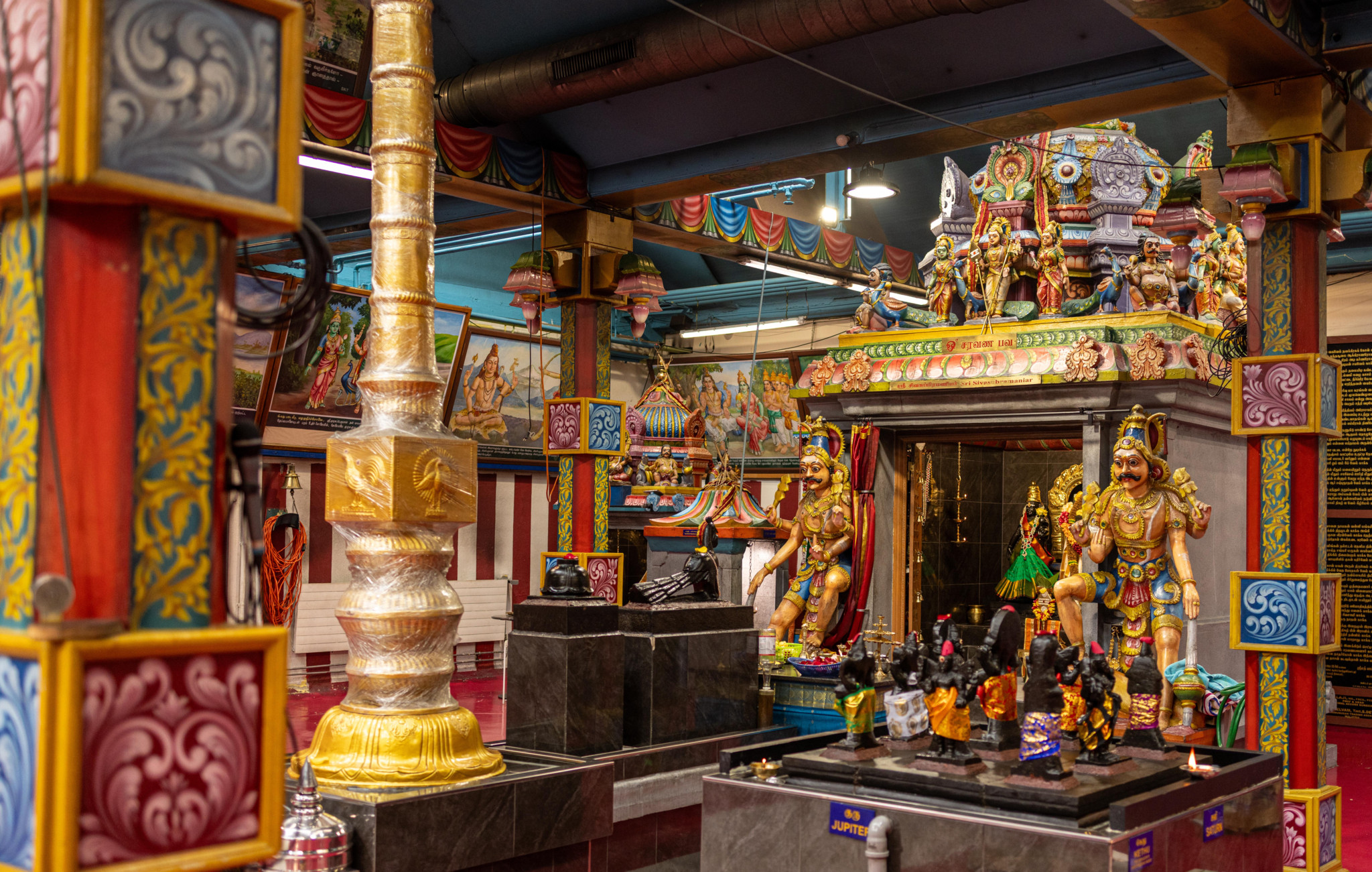 Farbenfroher hinduistischer Tempel mit goldenen Götterstatuen, reich verzierten Säulen und bunten Ornamenten in leuchtendem Rot, Blau und Gold.