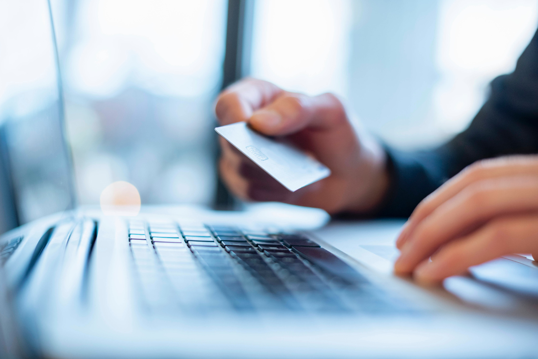 Main tenant une carte de crédit au-dessus d’un ordinateur portable pour un paiement en ligne.