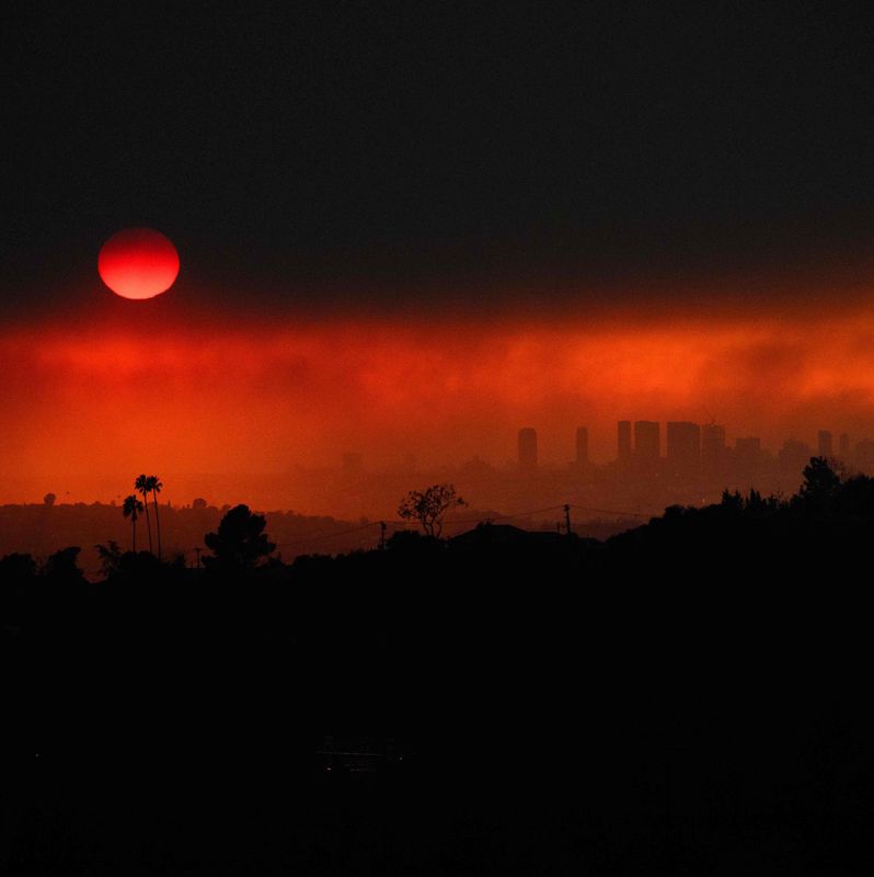 Vue aérienne montrant de la fumée des incendies, dont le Eaton Fire et le Palisades Fire, à Los Angeles, avec un ciel rougeoyant au coucher du soleil.