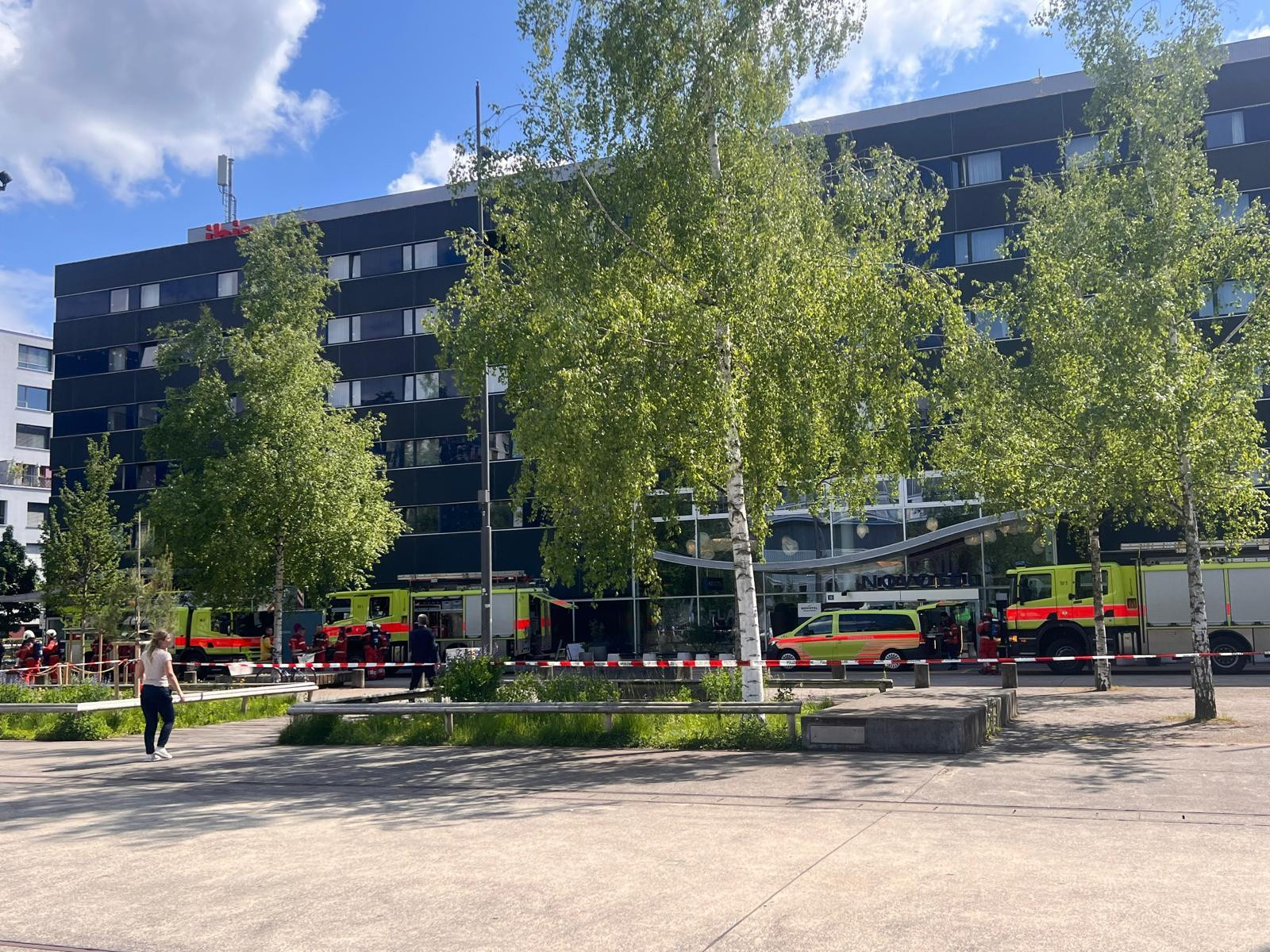 Mehrere Feuerwehrfahrzeuge vor einem modernen Gebäude mit Glasfassade, umgeben von Bäumen und einem abgesperrten Bereich.