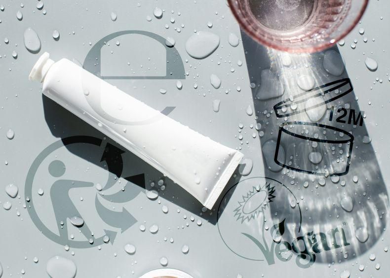 Tube de crème blanche sur une surface mouillée avec des symboles de recyclage, 12M et végan.