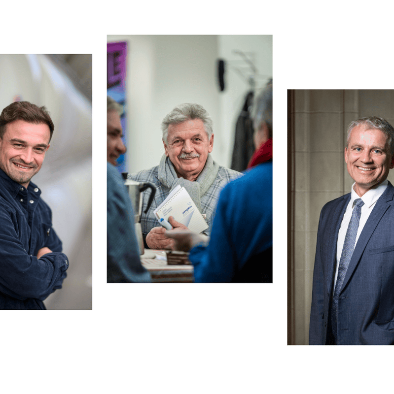 Drei Männer lächeln, zwei sehen direkt in die Kamera, ein Mann in einer Freizeitjacke und ein anderer in einem Anzug.