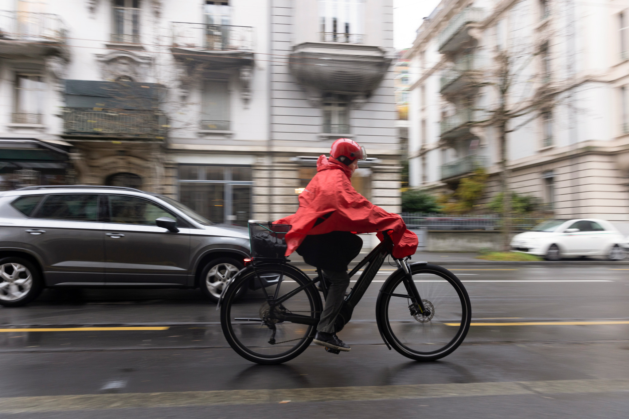 Cycliste portant un poncho rouge traverse l’Avenue d’Echallens à Lausanne, connu pour ses nombreux accidents de vélo.