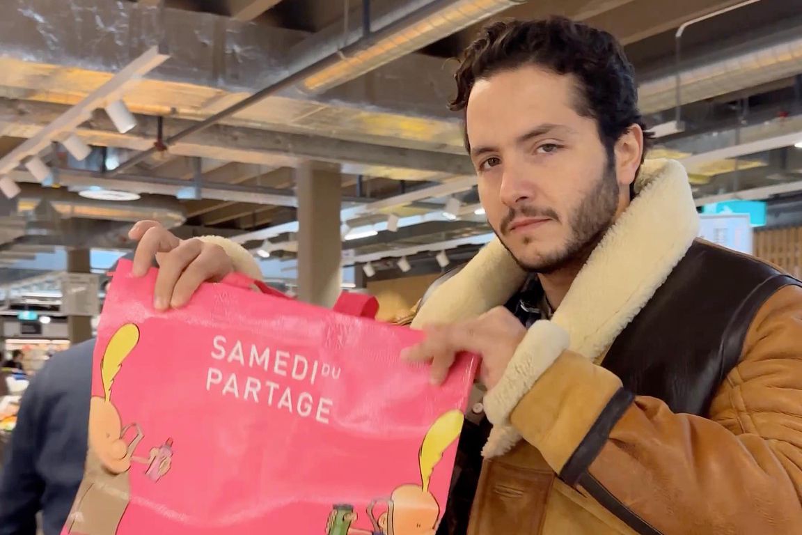 Homme tenant un sac rose avec l’inscription ’Samedi du Partage’ dans un supermarché.