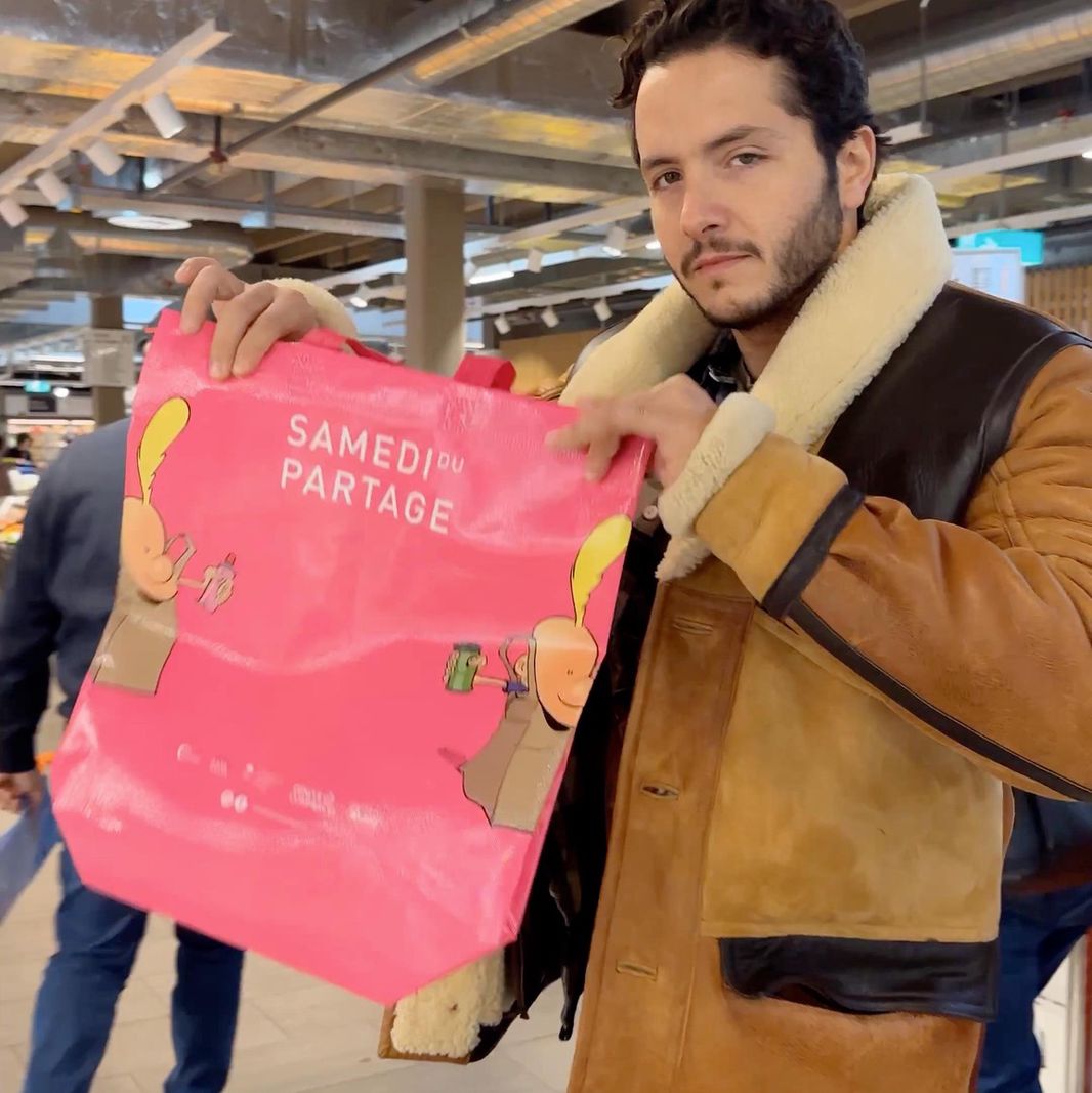 Homme tenant un sac rose avec l’inscription ’Samedi du Partage’ dans un supermarché.