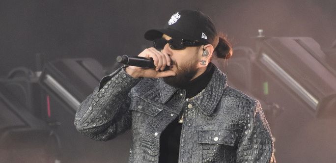 Le rappeur marseillais SCH en concert sur la Grande Scène des Eurockéennes de Belfort, vêtu d'une veste texturée et portant une casquette noire.