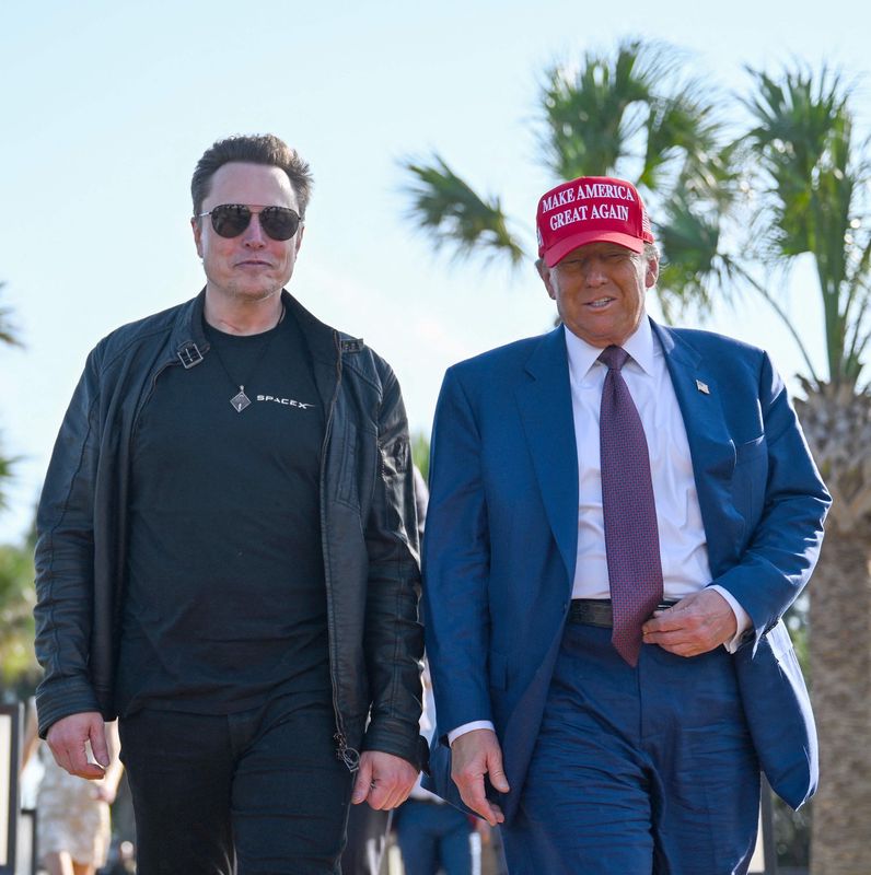 Donald Trump und Elon Musk gehen nebeneinander unter Palmen in Brownsville, Texas. Trump trägt eine rote ’Make America Great Again’-Kappe.