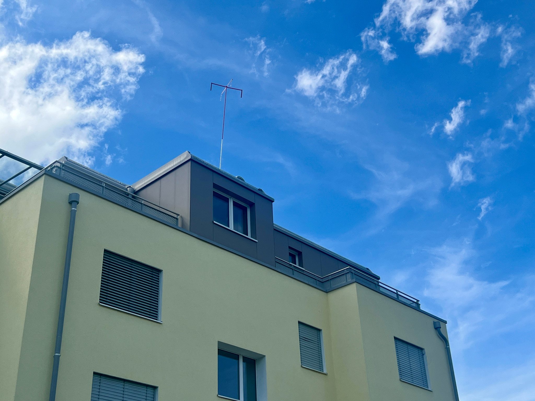 Modernes Wohngebäude mit gelber Fassade und Antenne auf dem Dach vor blauem Himmel mit Wolken.