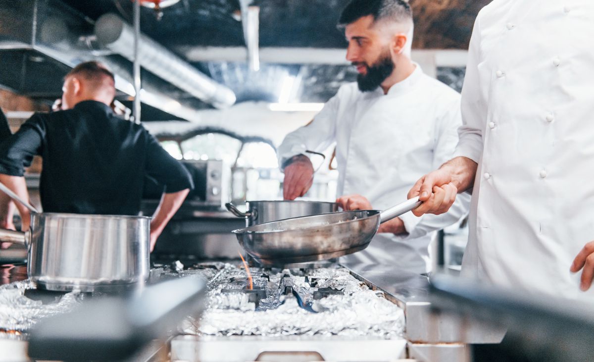 Des cuisiniers en uniforme blanc préparent des plats dans une cuisine professionnelle, lors d'une journée de travail chargée.