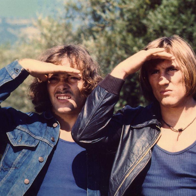 Deux hommes avec des vestes en jean regardant au loin avec des mains en visière, devant un paysage naturel.