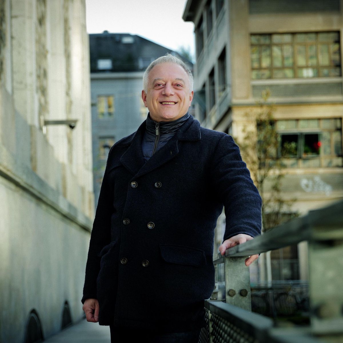 Portrait de Philippe Olza, metteur en scène, à Genève, le 8 janvier 2025, se tenant sur un pont avec des bâtiments en arrière-plan.