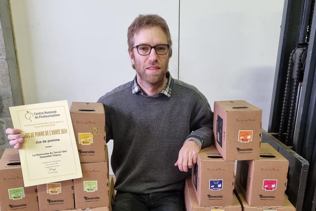 Homme assis sur une palette avec des boîtes de jus de pommes, tenant un diplôme de l’Office Romand de Lutte Bio
