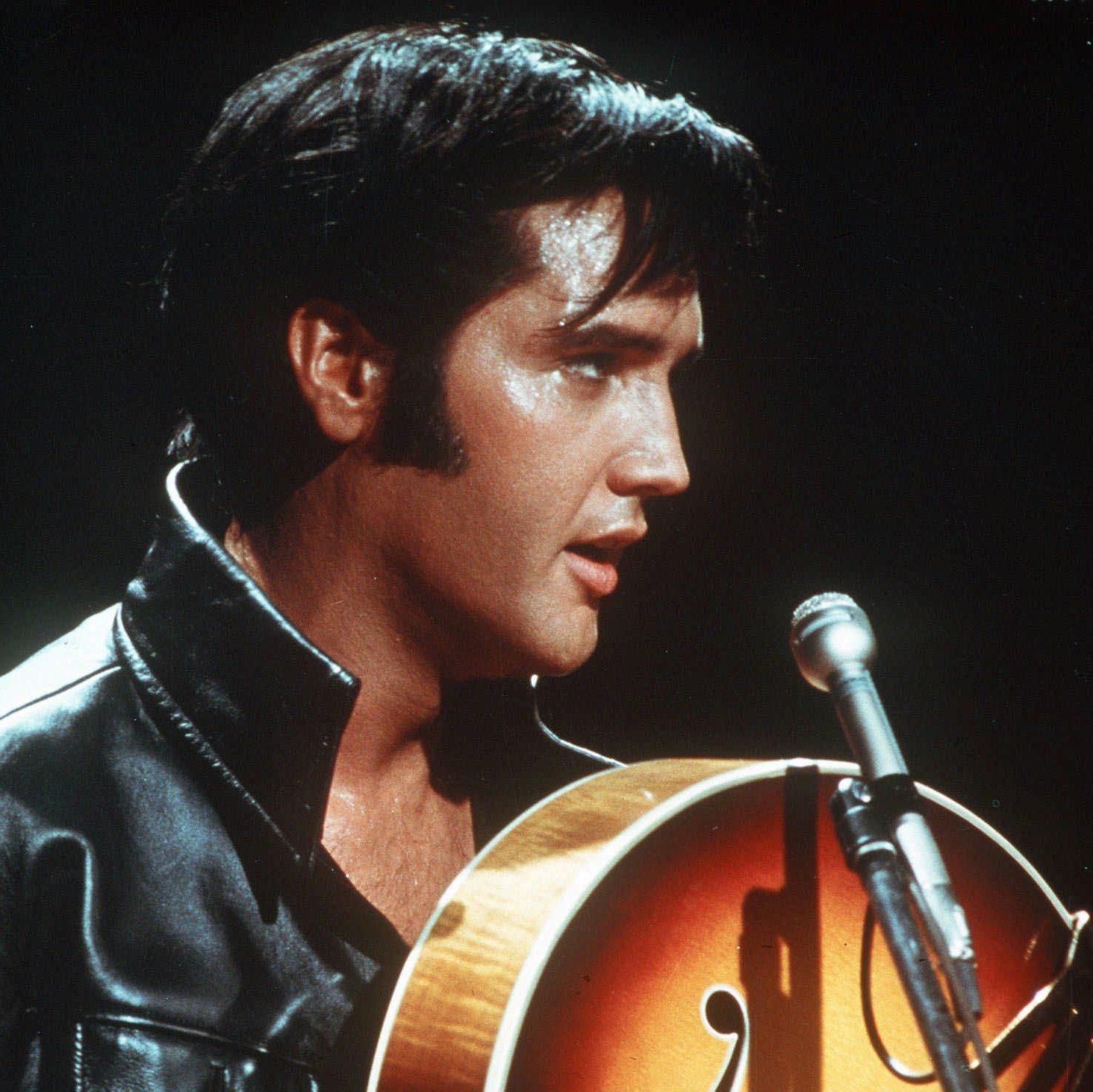 Elvis Presley en 1968 jouant de la guitare, illustrant son style emblématique de rock ’n’ roll avec une veste en cuir.