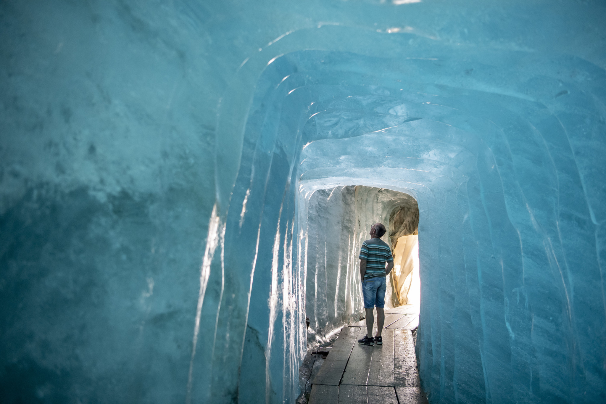 Besucher in der Eisgrotte des Rhonegletschers am Furkapass, umgeben von blau schimmernden Eiswänden, Juli 2022.