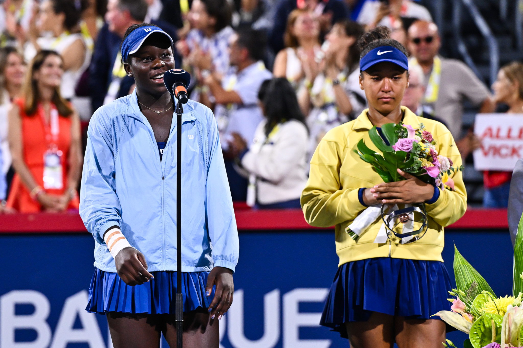 Victoria Mboko spricht nach ihrem Sieg im Damenfinale gegen Naomi Osaka beim WTA 1000 National Bank Open in Montreal. Osaka hält einen Blumenstrauss.