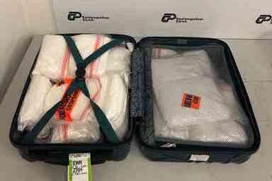 Offener Koffer mit mehreren in Plastik verpackten Gegenständen auf einem Tisch.