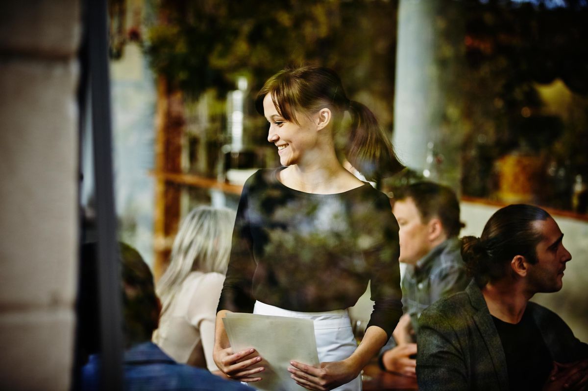 Serveuse souriante prenant une commande, vue à travers une fenêtre d’un café.