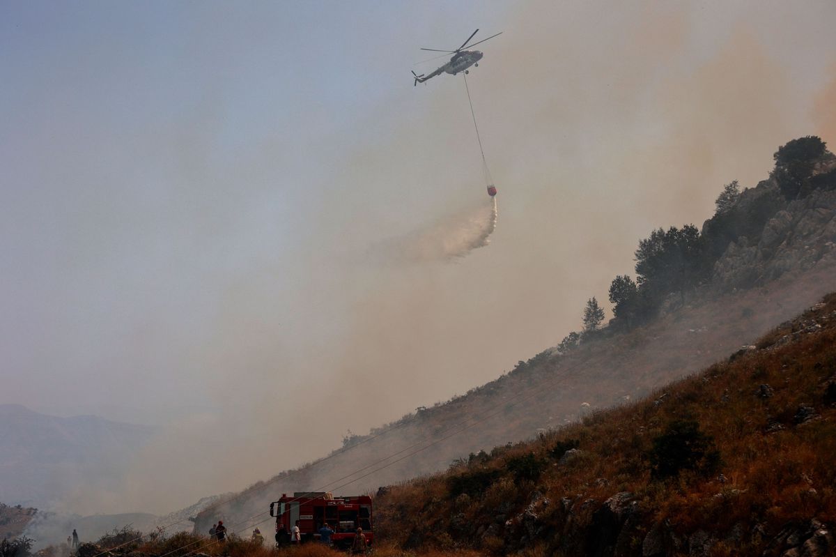 L’île de Corfou, très prisée des touristes, subit à son tour un intense incendie de forêt. Un hélicoptère largue de l'eau sur un site en feu, ce lundi 24 juillet.