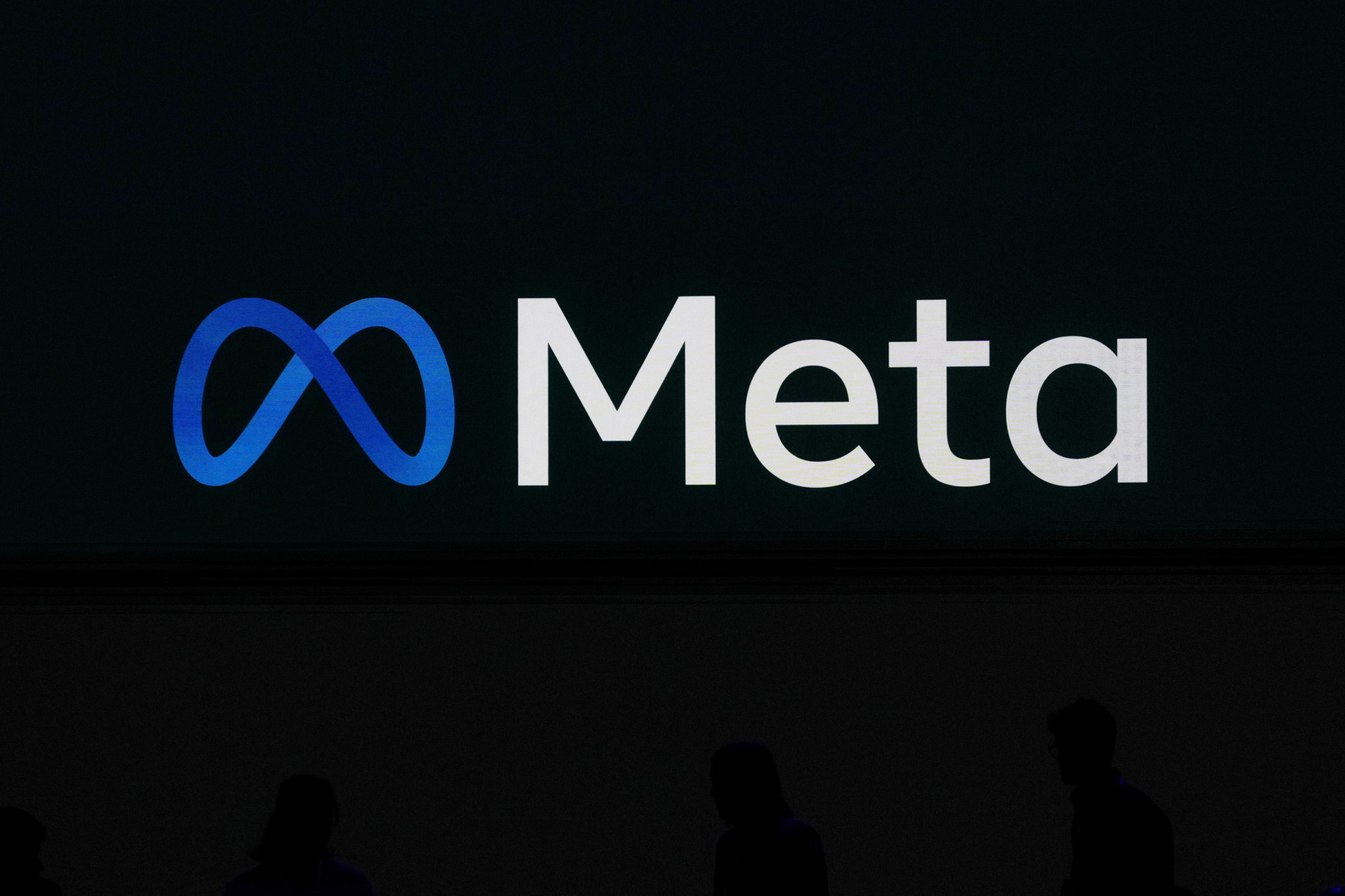 Meta-Logo auf einem Videobildschirm an der LlamaCon 2025 in Menlo Park, Kalifornien, mit Silhouetten von Personen im Vordergrund.