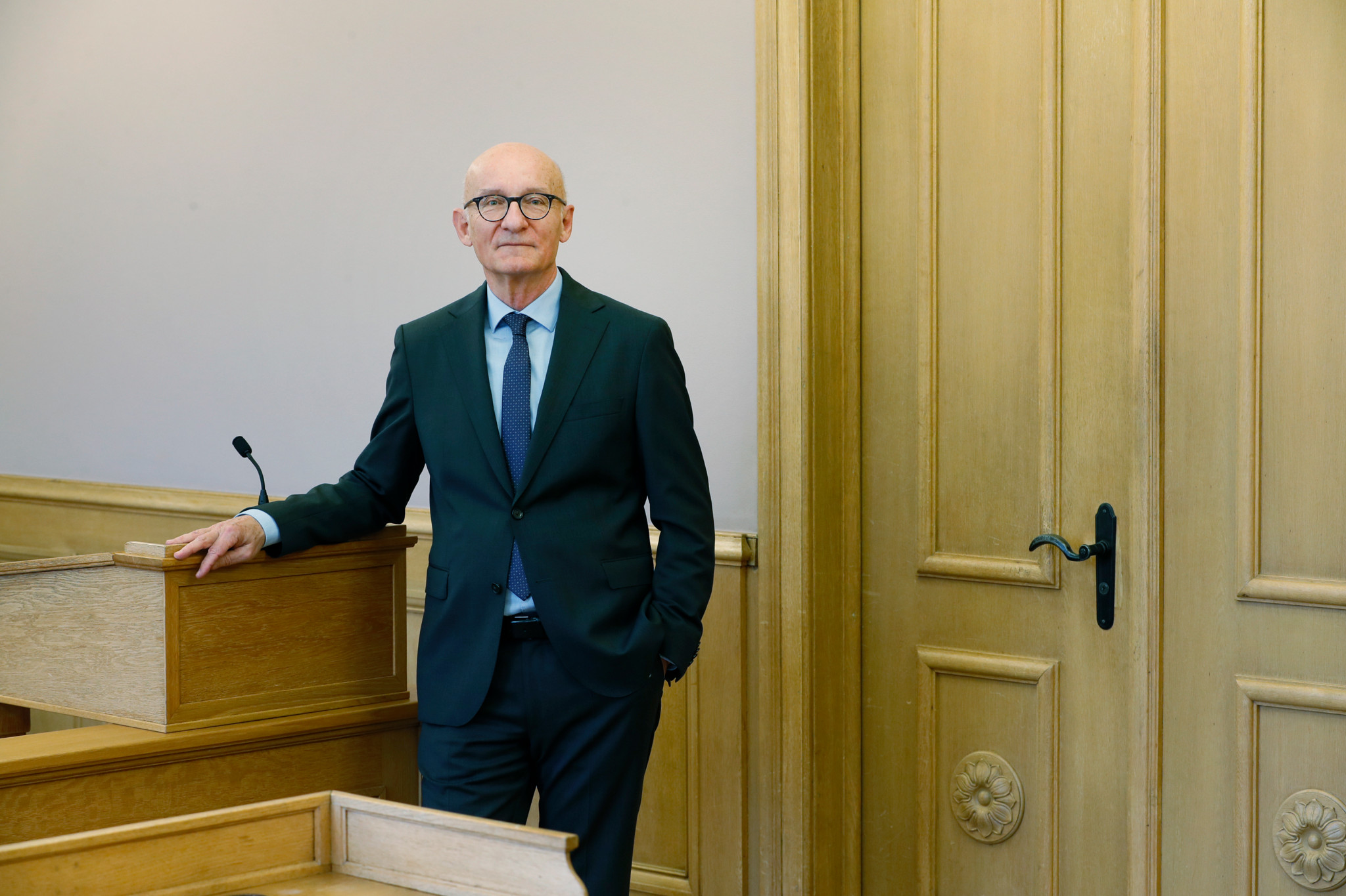 Präsident Rainer Hohler des Bezirksgerichts Bülach steht in einem Gerichtssaal neben einem Rednerpult. Er trägt einen Anzug und eine Krawatte und blickt in die Kamera.