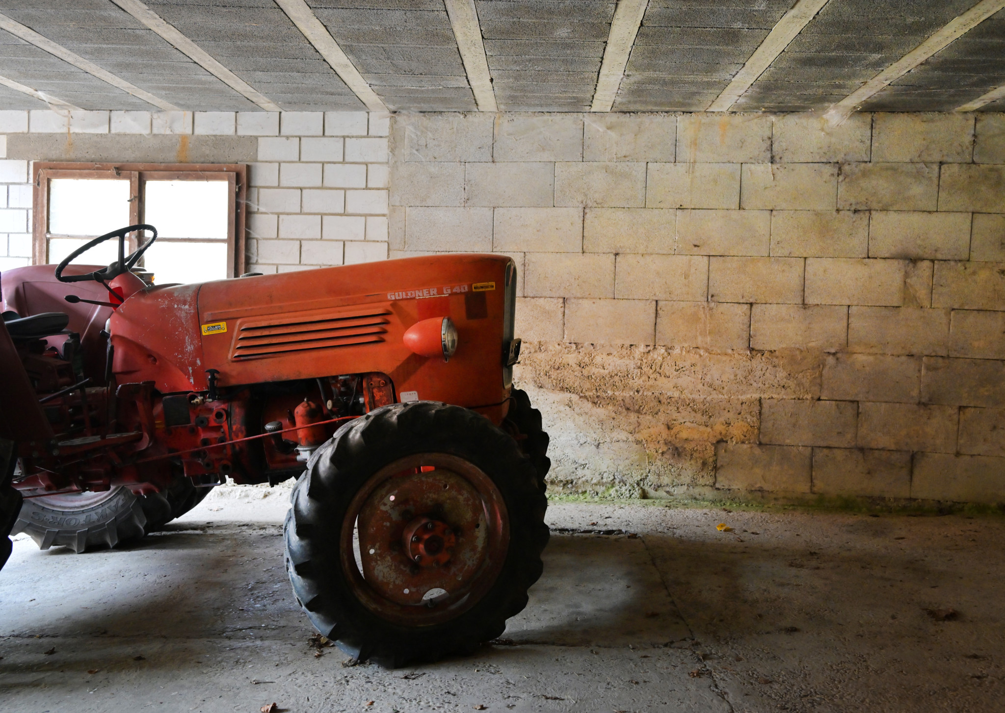 Roter Traktor in einer alten Scheune mit Steinmauern – Symbol für Baukultur und ISOS-Schutzbestimmungen in der Schweiz.