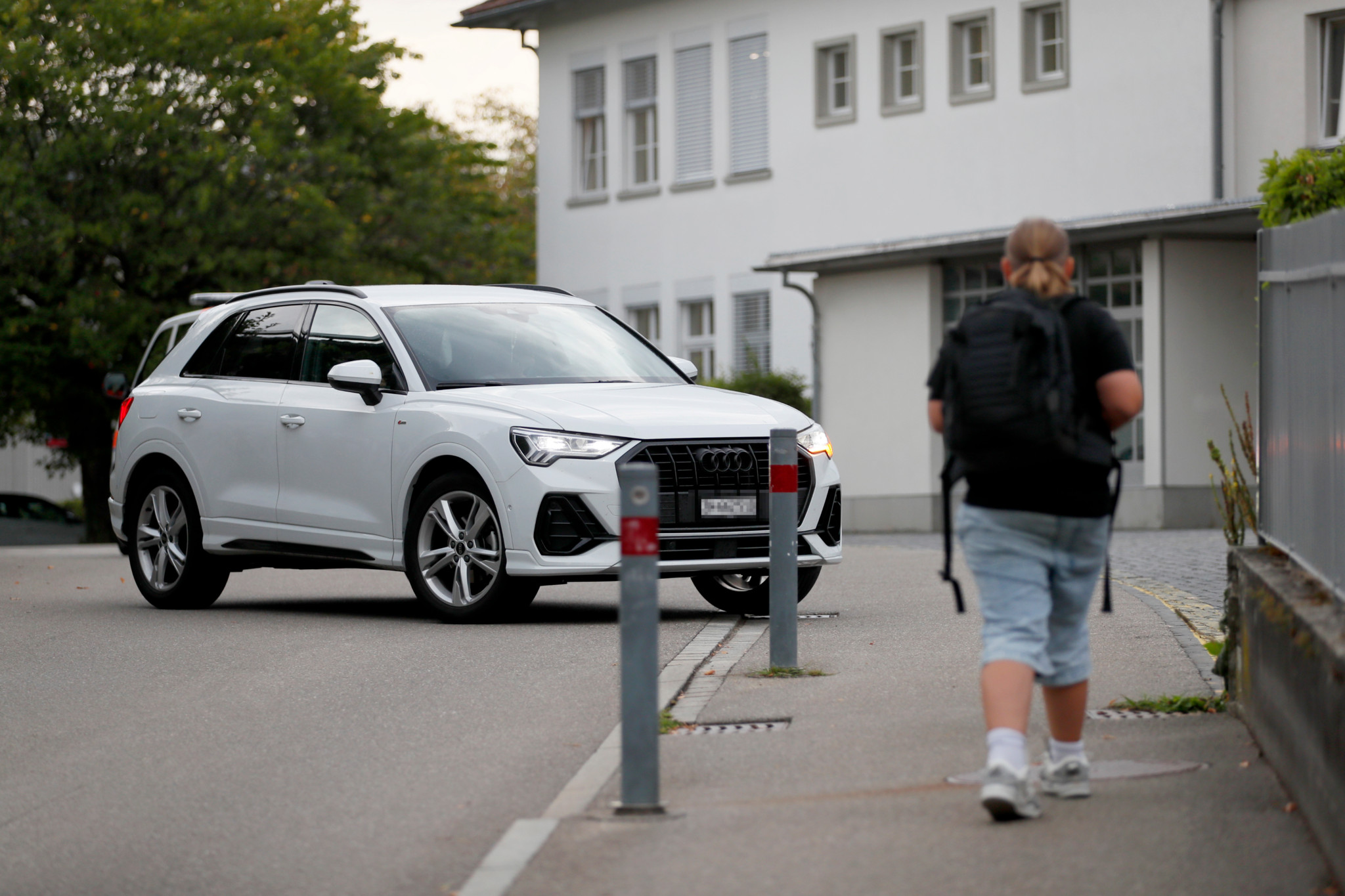 Elterntaxi vor der Schule Kirchbühl Nord in Stäfa: Weisser Audi SUV parkiert, während ein Kind mit Rucksack zur Schule läuft.