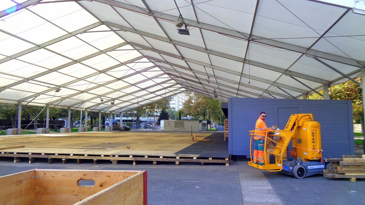 Construction d'une grande tente blanche avec des ouvriers en tenue orange utilisant une plateforme élévatrice.